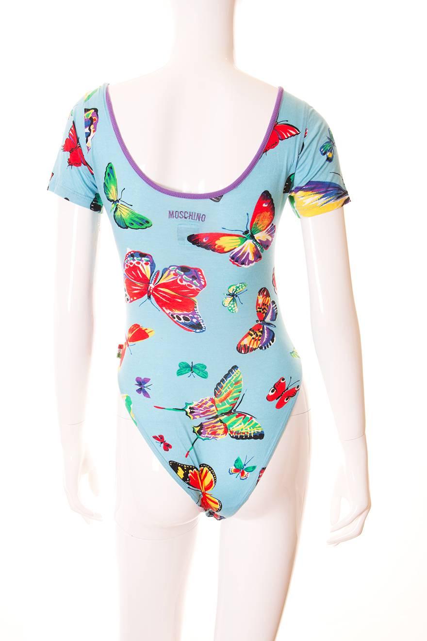 The print on this Moschino bodysuit is truly lovely. Sky blue fabric with butterflies all over in an array of bright hues. U neck with contrast purple piping. Moschino logo embroidered at the back of the bodysuit. High cut leg. Circa 90s.

This