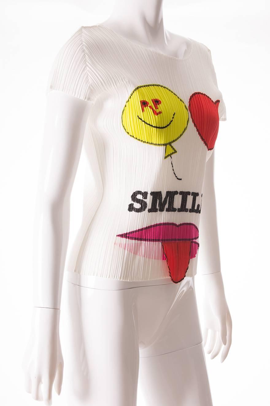 This top by Issey Miyake is in his signature pleated fabric.  The top features a smiling balloon and a love heart printed at the top, as well as a pair of lips with a tongue hanging out of them.  There is a faint imprint of this design at the back