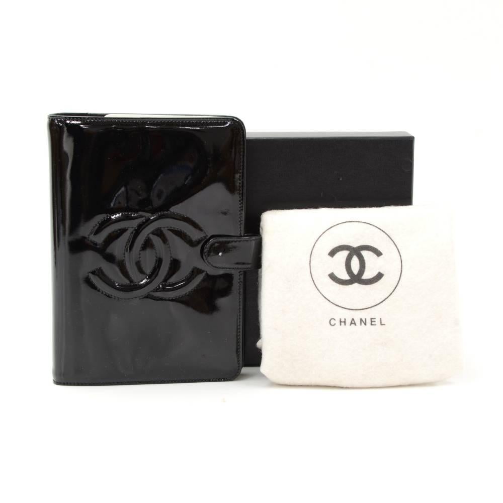 Chanel agenda in black patent leather. It has famous CC logo stitched onto the front and access secured with a stud closure. Inside has 1 open pocket and 1 pen holder. Comes with 6 rings styled in gold tone. Absolutely gorgeous and stylish. 

Made