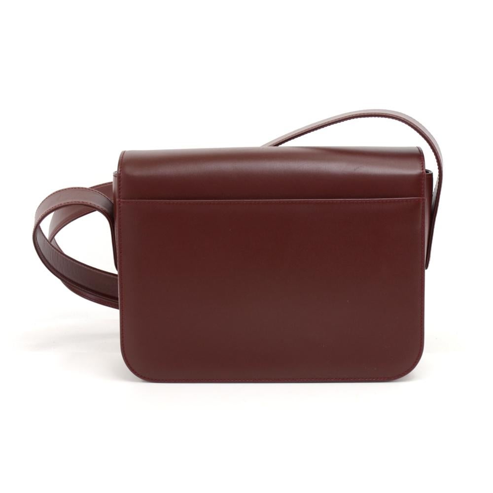 Catier Must Line shoulder bag in burgundy leather. It has twist lock on the front flap with the Cartier logo  and 1 open slip in pocket on the back. Inside lining is in burgundy fabric with Cartier monogram. It has a front slip pocket compartment