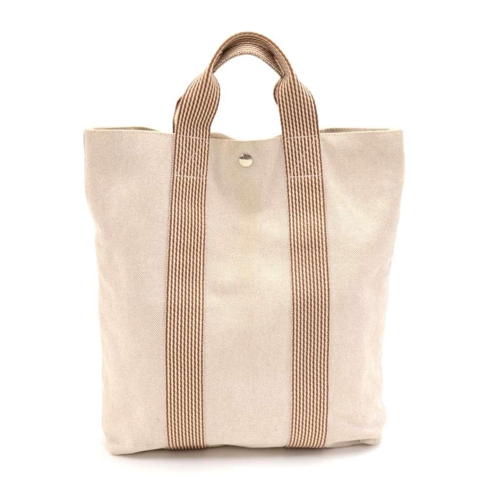 Hermes Beige Tote Bag. Made with beige canvas and a beige and brown striped support canvas handles. The front has 3 convenient and large pockets. The top is secured with a silver tone snap button engraved with 