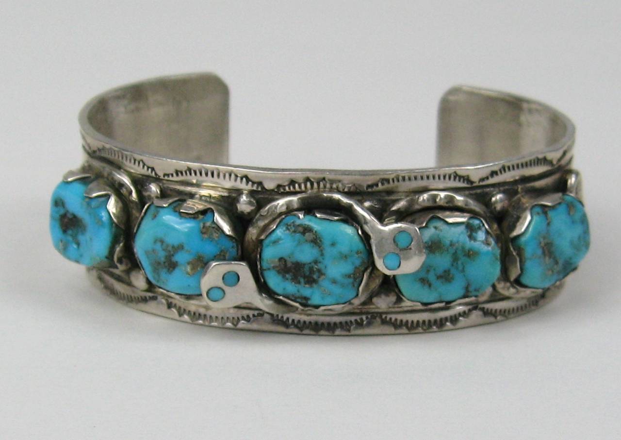 Two snakes wrapping themselves around the center Turquoise stone 
Bracelet has 5 stones
Measures .77