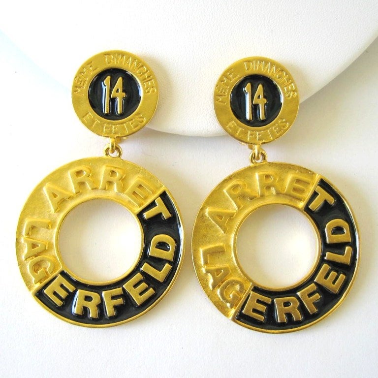 These are vintage Karl Lagerfeld gold tone hoop earrings. Purchased and stored away.  They read on the front: Meme Dimanches Et Fetes 15 Arret Lagerfeld. On the backs: 14 Blvd De La Madeleine. Enamel and Gold tone finish They measure 2.75 top to