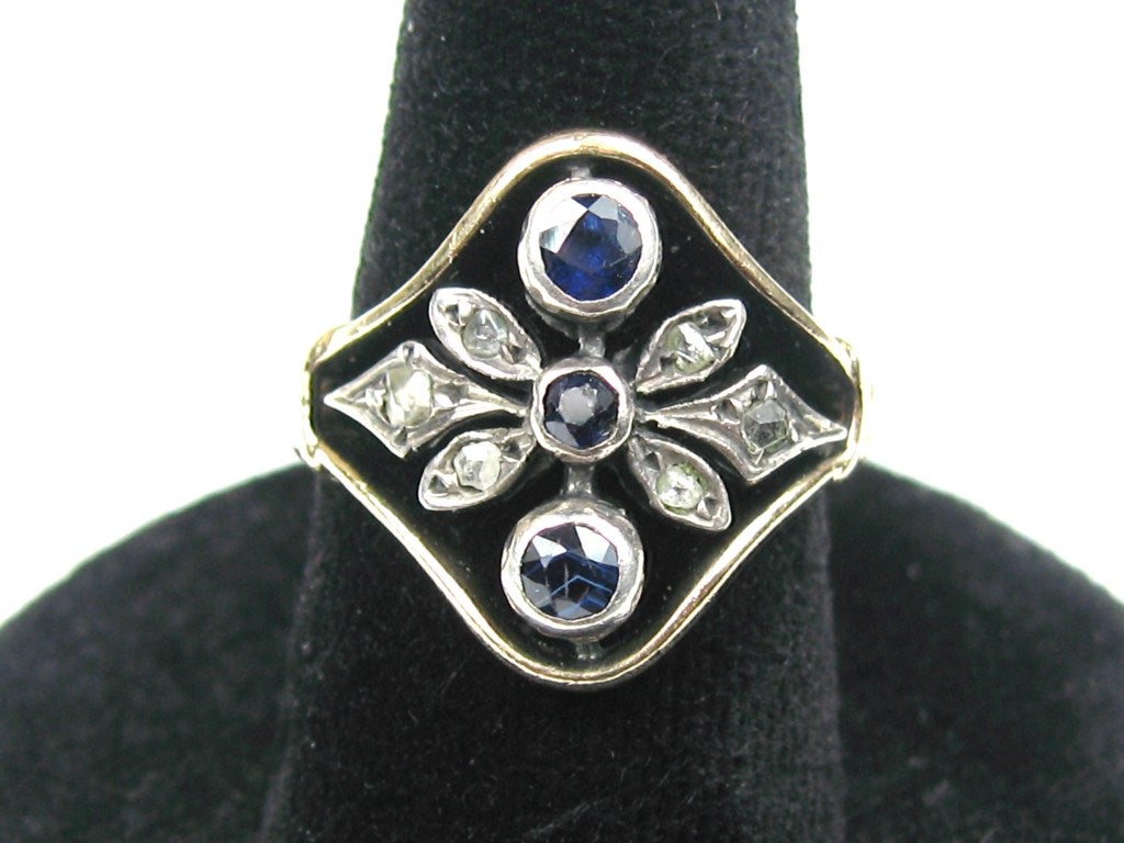 A wonderful Antique Sapphire Ring with Diamond Accents. Hallmarked 500 which is less than 14K more like 12K. The Sapphires are Bezel set and has minor wear. Mine Cut diamonds set like petals are both sides of the shank. 3 Sapphires, and 6 Diamonds.