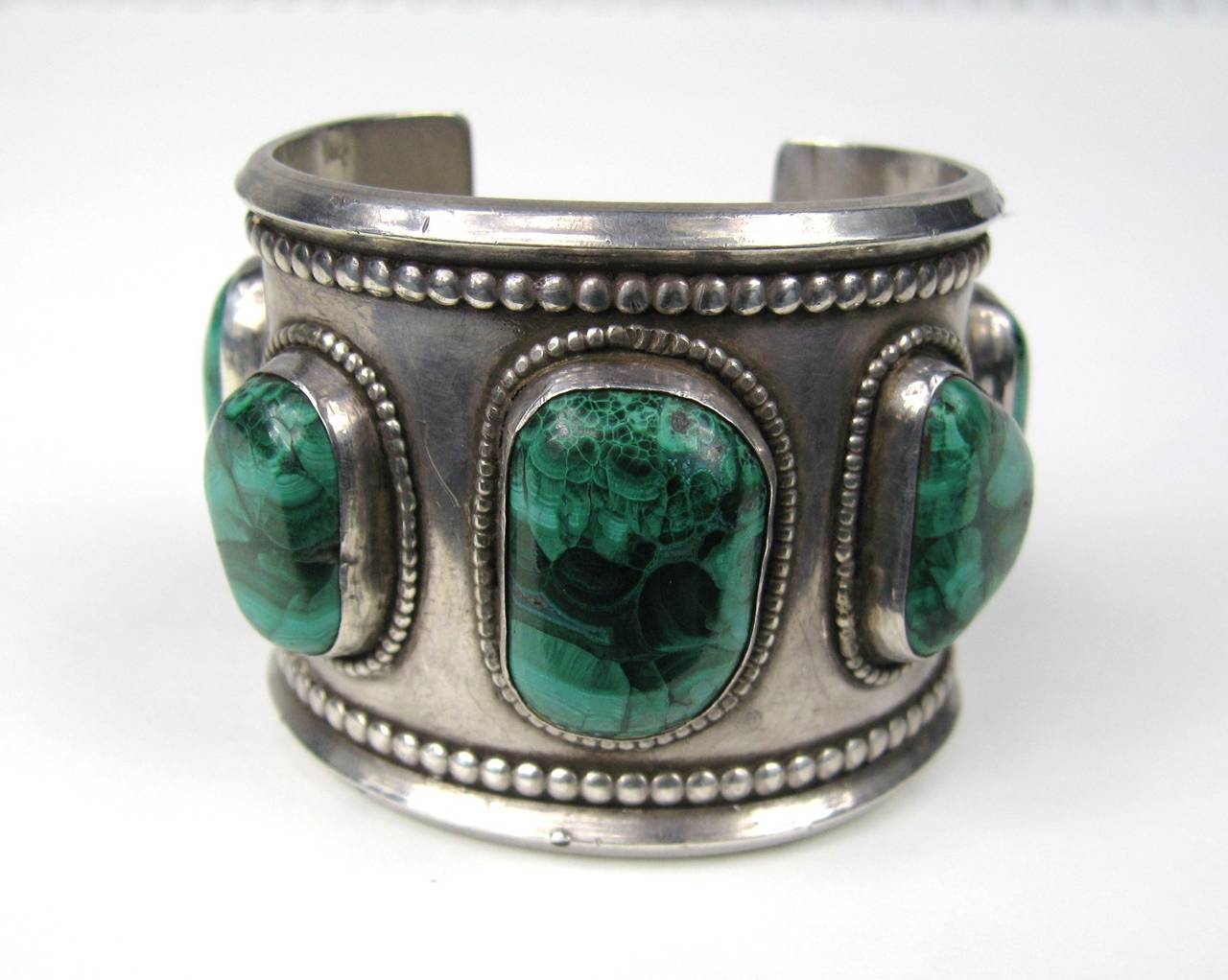 Massive bracelet with large scale Malachite stones set in this one. It measures 2.05 in wide 1.11 in x .76 in largest stone in the center 1.14 in opening will fit a size 6-7 in wrist and does have a bit of give. This is out of a massive collection