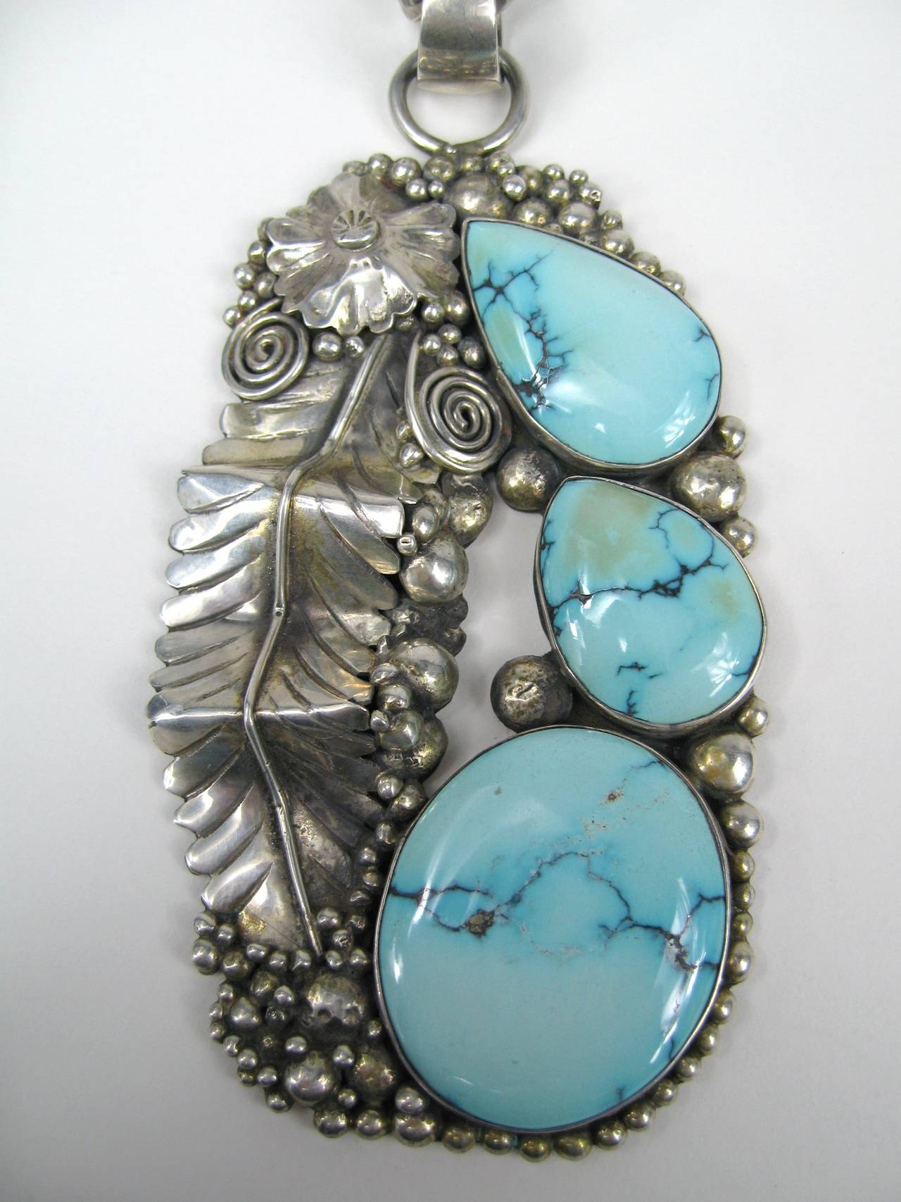 Stunning Turquoise on this handmade piece of Native American Jewelry.  Large in scale. 3 pieces of Turquoise set in an elaborate leaf pendant
Measuring 4.28 inches long x 2.21 inches width. Hanging from a link chain that measures 23 inches long.
