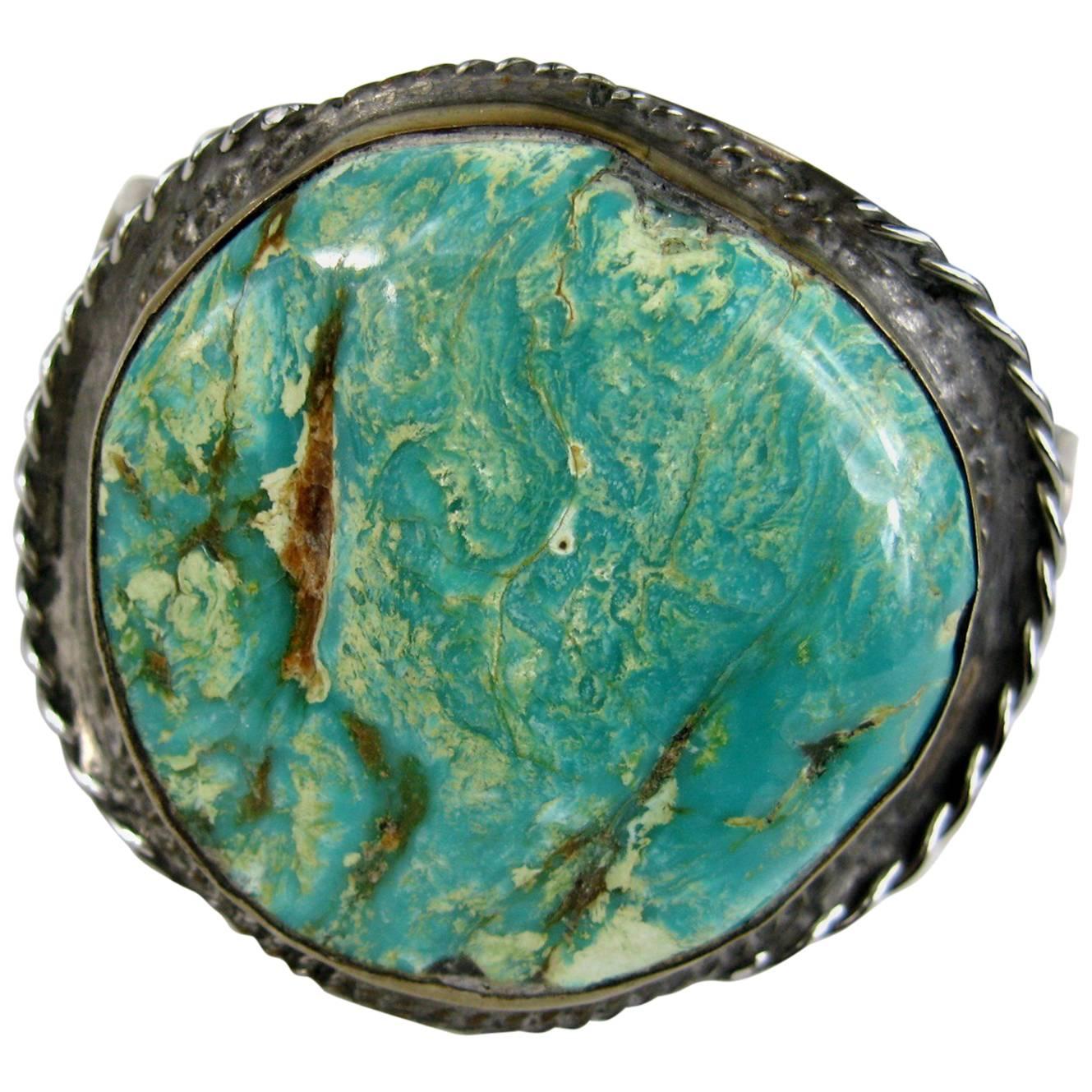 Early hand crafted Navajo Turquoise Cuff Bracelet which features a very large stone, measuring approximately 1.82 inches x 1.82 inches. Set in a Silver 3 ring Cuff bracelet. Hallmarked on the back with a image of a bird. Measuring 2 inches top to