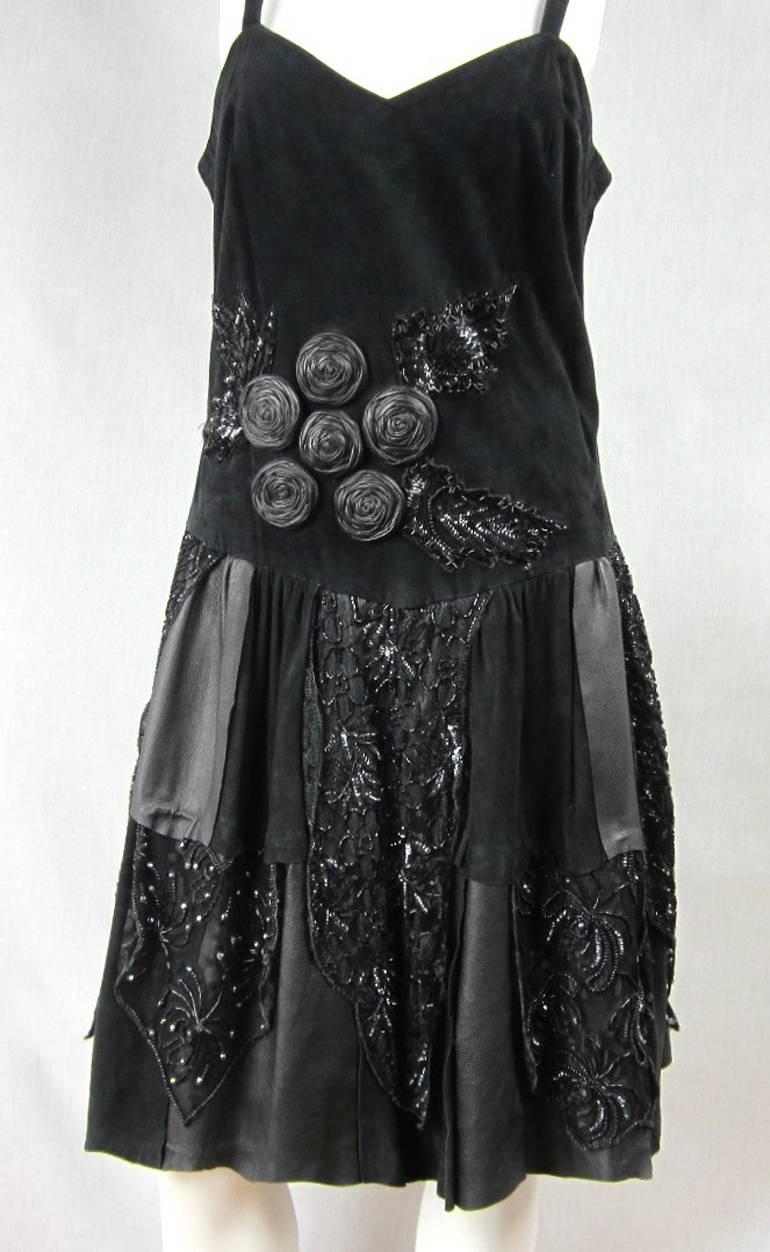 Cuero negro de los años 80, encaje y lentejuelas. Vestido con cintura caída. Tiene abalorios cosidos a mano y cremallera en la espalda. Grandes rosetas redondas de cuero en la parte delantera. Parches de ante y cuero.  Es una versión divertida de un
