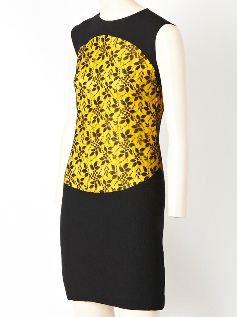 James Galanos, wool crepe, silk and lace cocktail dress. Dress is fitted, with a black wool crepe body. There is an oval panel starting just below the shoulder level and continues below the hip. The panel has an under layer of yellow silk and an