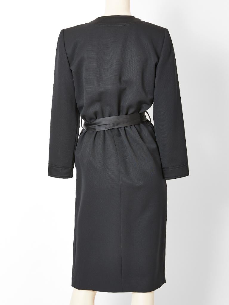 Yves Saint Laurent, Rive Gauche, black faille cocktail dress, having satin edging detail and a black satin bow at the waist. Dress has side button closures embellished with round, black enamel and rhinestone buttons.