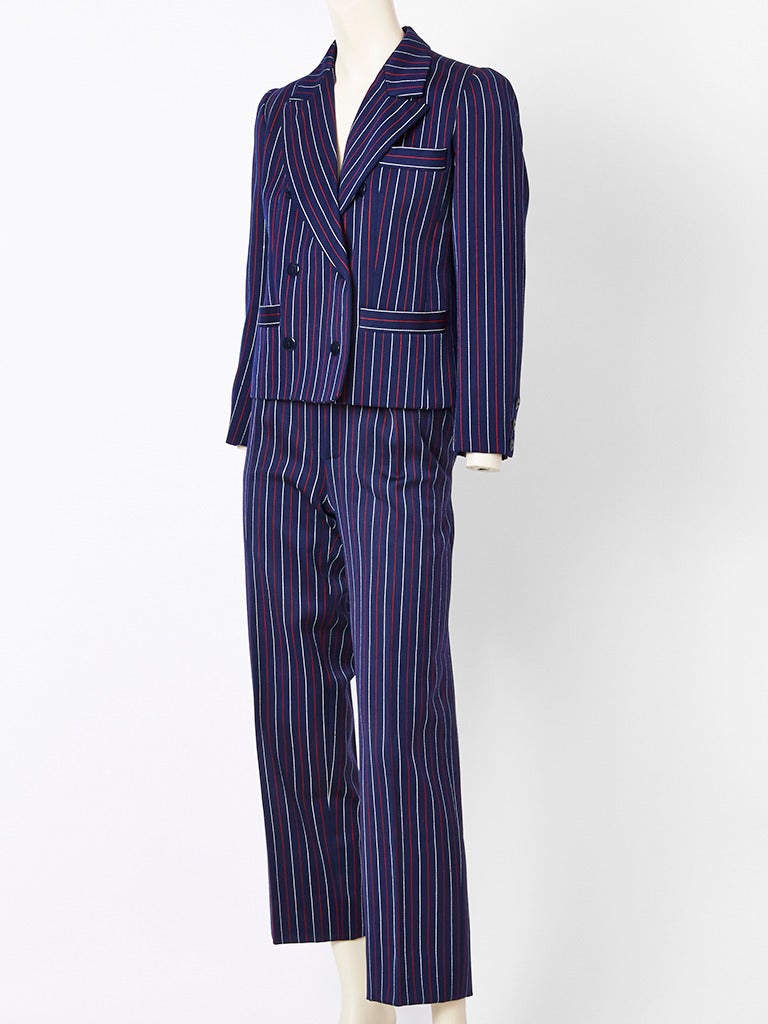 Yves Saint Laurent, navy blue, wool, pinstripe pant suit. Navy ground with red and white pinstripe. Jacket is double breasted with pockets and falls at the hip.
Pant is straight leg.