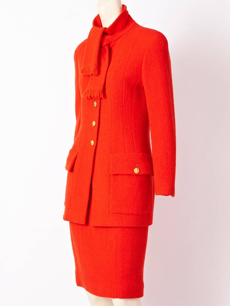 Chanel, red, wool boucle, suit . Jacket is fitted with an attached scarf that ties at the neck, Jacket ends by the thigh with deep pockets. Signature, gold Chanel buttons.
