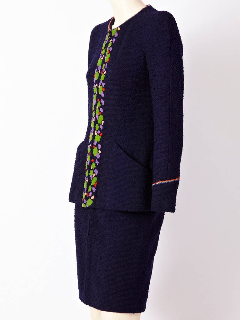 Navy blue, wool boucle, collarless suit with zipper front and abstract, floral appliques down the center front. Printed trim at the wrist.