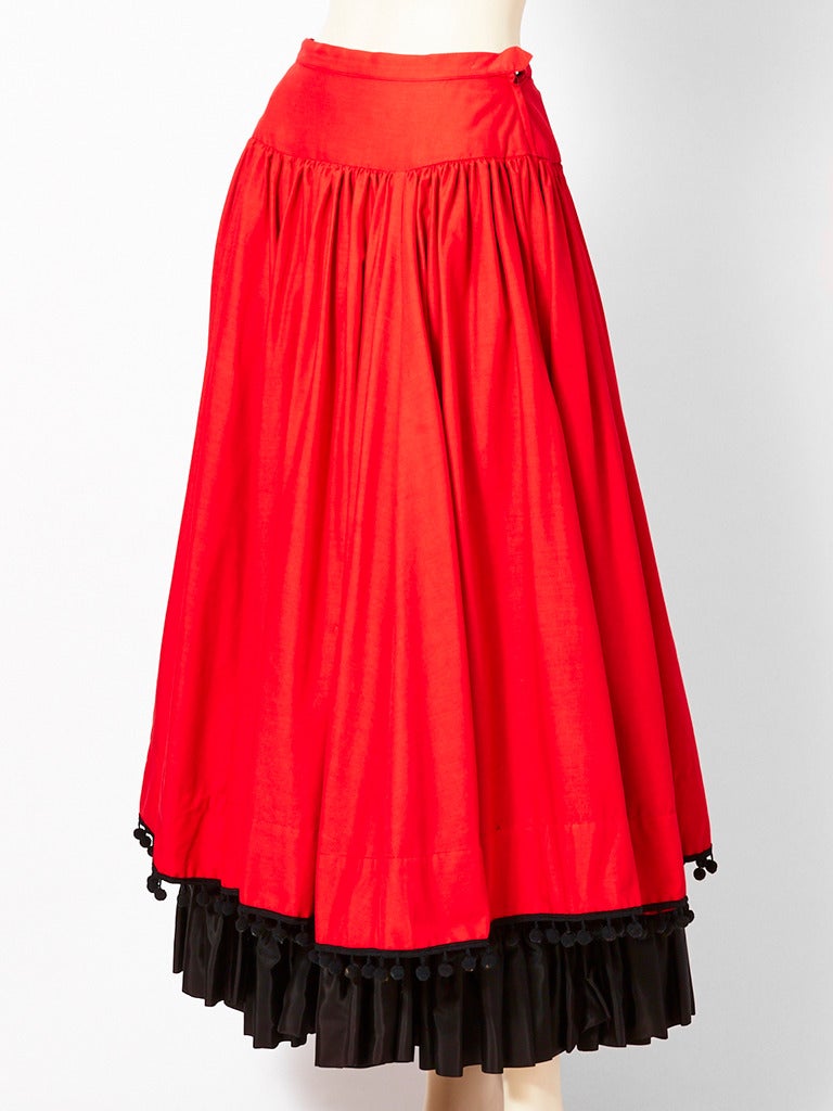 Yves Saint Laurent, red and black gypsy skirt from the late 70's. Skirt has a  dropped waist, with full gathering. Skirt is edged in black pom poms. There is a 6 inch, black taffeta, ruffle layer coming out from the hem of the skirt.