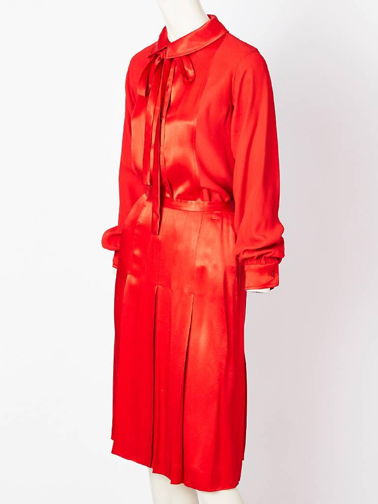 Yves Saint Laurent, rive gauche red satin back crepe top and pleated skirt.
Top has a pleated collar with a detatchable tie having the shiny side of the crepe front panels, while the rest is a matte crepe. Pleated skirt is shiny.