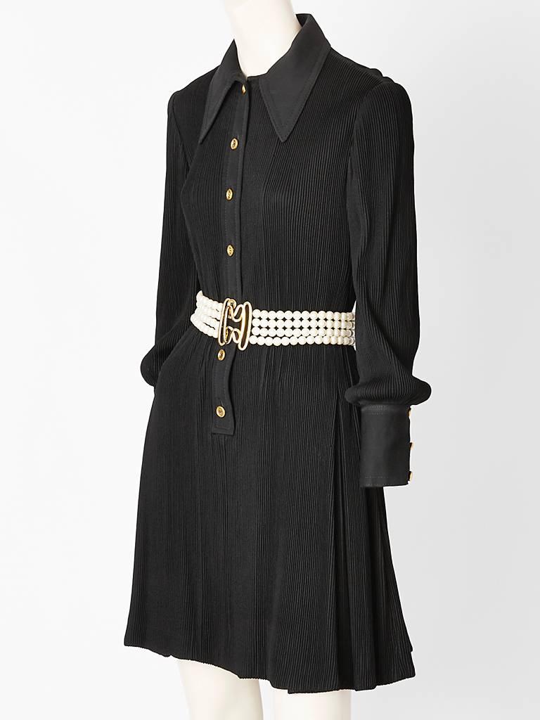 Galanos, black, shirt dress with a texture of fine, thin vertical ribbing on the entire surface of the dress, excluding the collar, cuffs, and placket for the buttons.
Skirt of the dress has hidden, box pleats that start below the hip. The dress