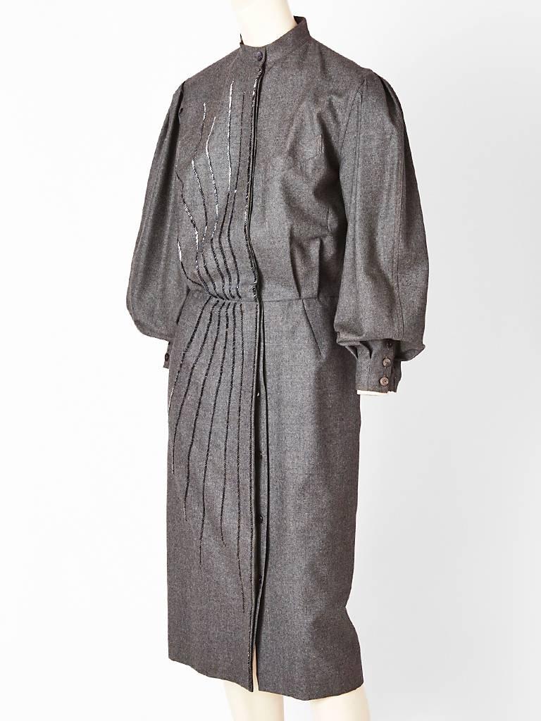 Gucci, gray flannel, wool, shirt dress, with mandarin collar and hidden front buttons. Dress is embellished with gunmetal bugle beads making an asymmetric
design on one side only. Full sleeves that end in a cuff. C. 1980's.