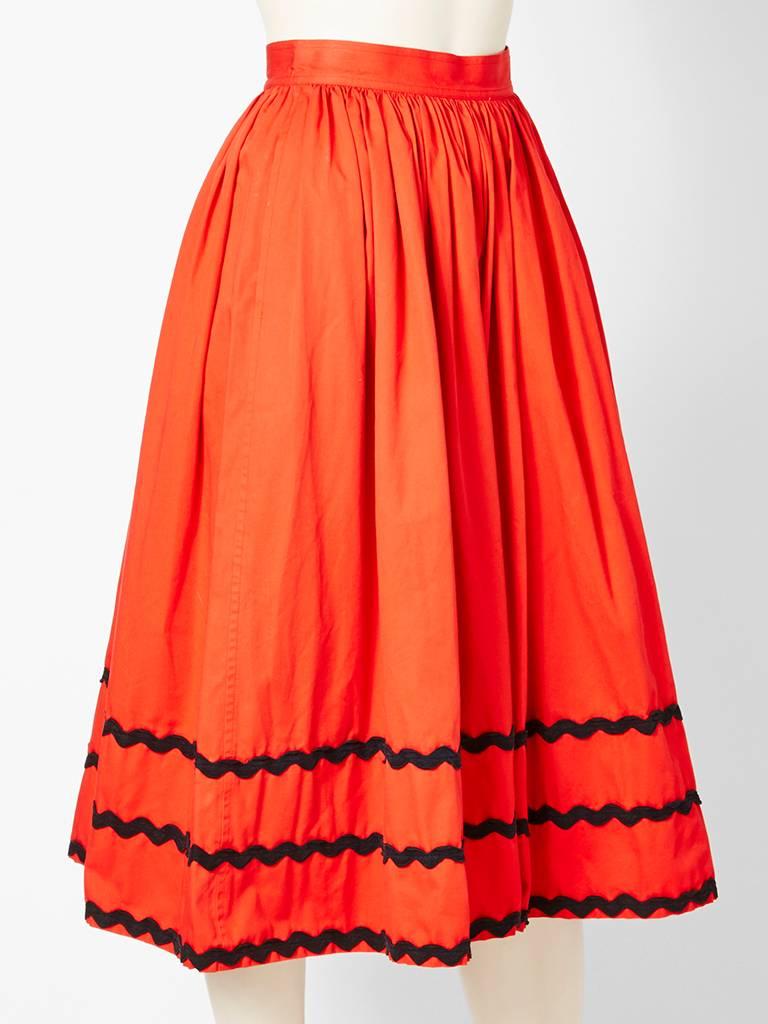 Yves Saint Laurent, Rive Gauche,  orangey-red,  cotton, gathered skirt with black ric rac trim detail at the hem. C. 1970's Deep hidden pockets by the hips.