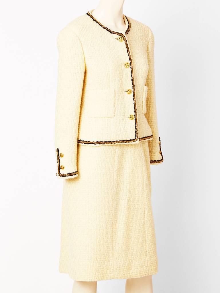 Chanel, ivory, wool boucle, classic (Coco Chanel), suit with external, gold chain, and black wool trim. Skirt is A line. C. 1980's.