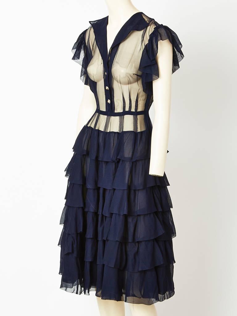 Navy, chiffon dress made in a custom dress shop in New York in 1949.
Bodice is fitted with ruffle detail at the shoulders and sleeves. Collar is pointed.
Faux pearl buttons. Skirt has tiers of ruffles.