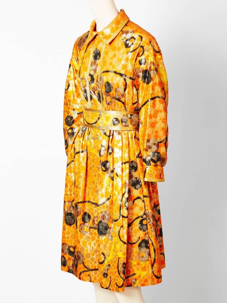 Geoffrey Beene, orange brocade,patterned dress with gold lame thread detail. Dress has a pointed collar, long full sleeves, ending in a tight buttoned cuff, slightly high waist with gathered skirt and matching wide self belt.