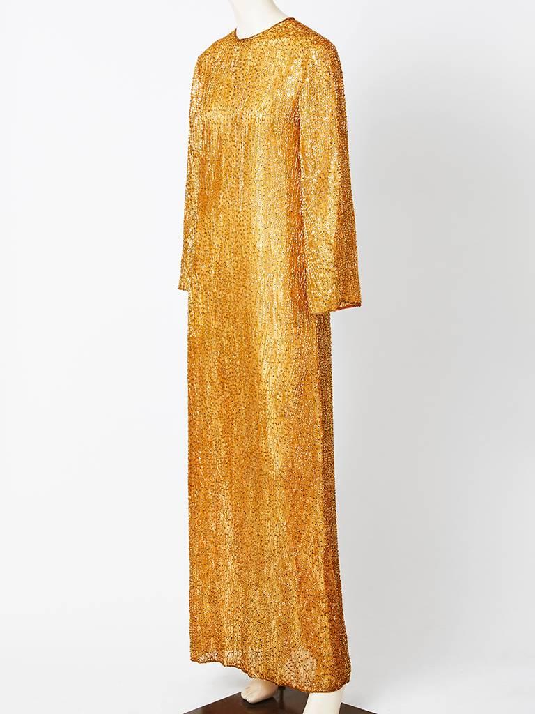 Halston, Amber toned, chiffon, sheath like evening gown entirely encrusted in bugle beads. Lines in silk with a jeweled neckline and long slim sleeves.
