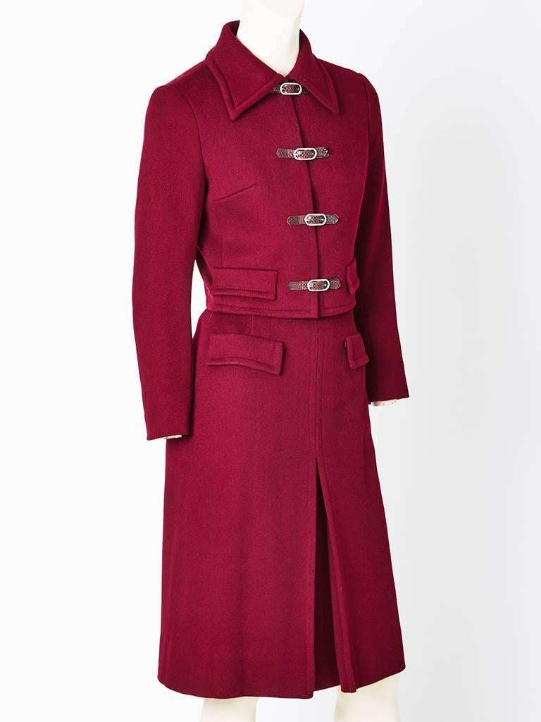 Jaeger, burgundy, wool, skirt suit having a fitted cropped jacket that ends at the waist. Collar is pointed, with faux flap pockets, and lizard and metal buckle closures detail. Skirt is slightly A line with a center inverted pleat and repeated flap