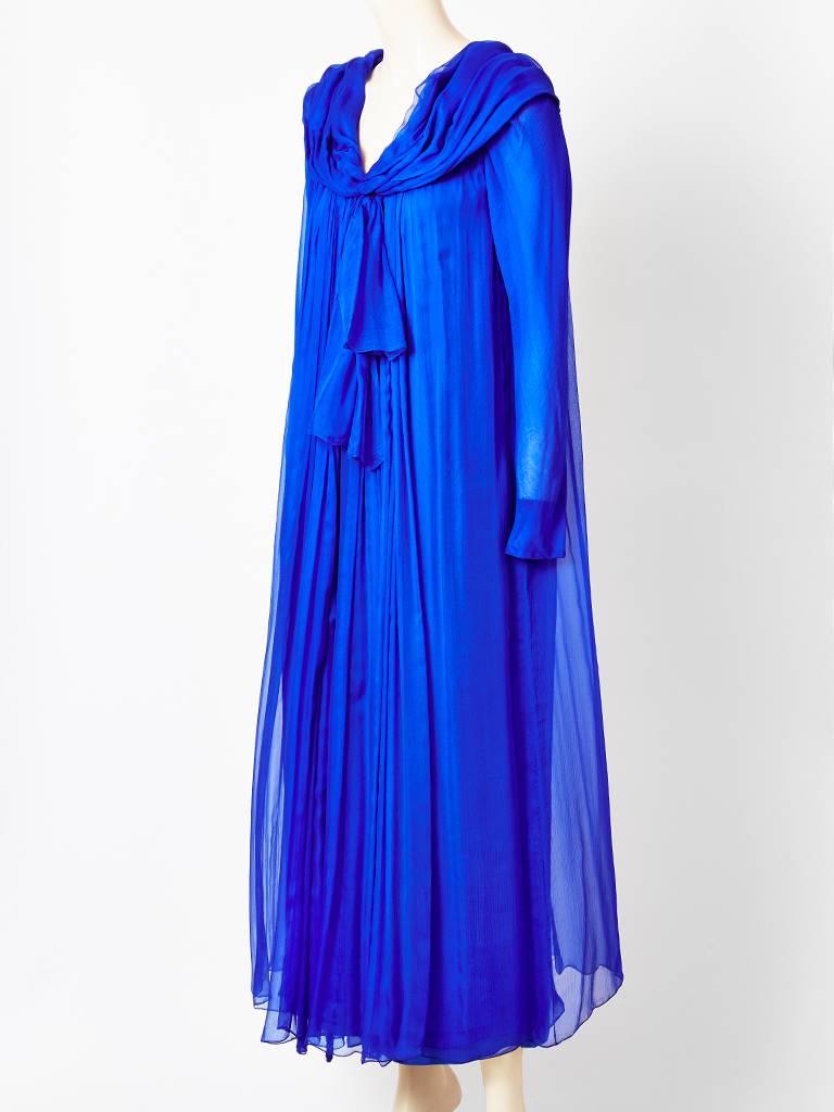 Yves Saint Laurent Couture, cobalt blue, layered, mousseline de sole, evening dress, having long sheer sleeves, a draped collar with a bow, that sits on the  shoulders and turns into a hood. Dress is gathered from the shoulders having soft sheer