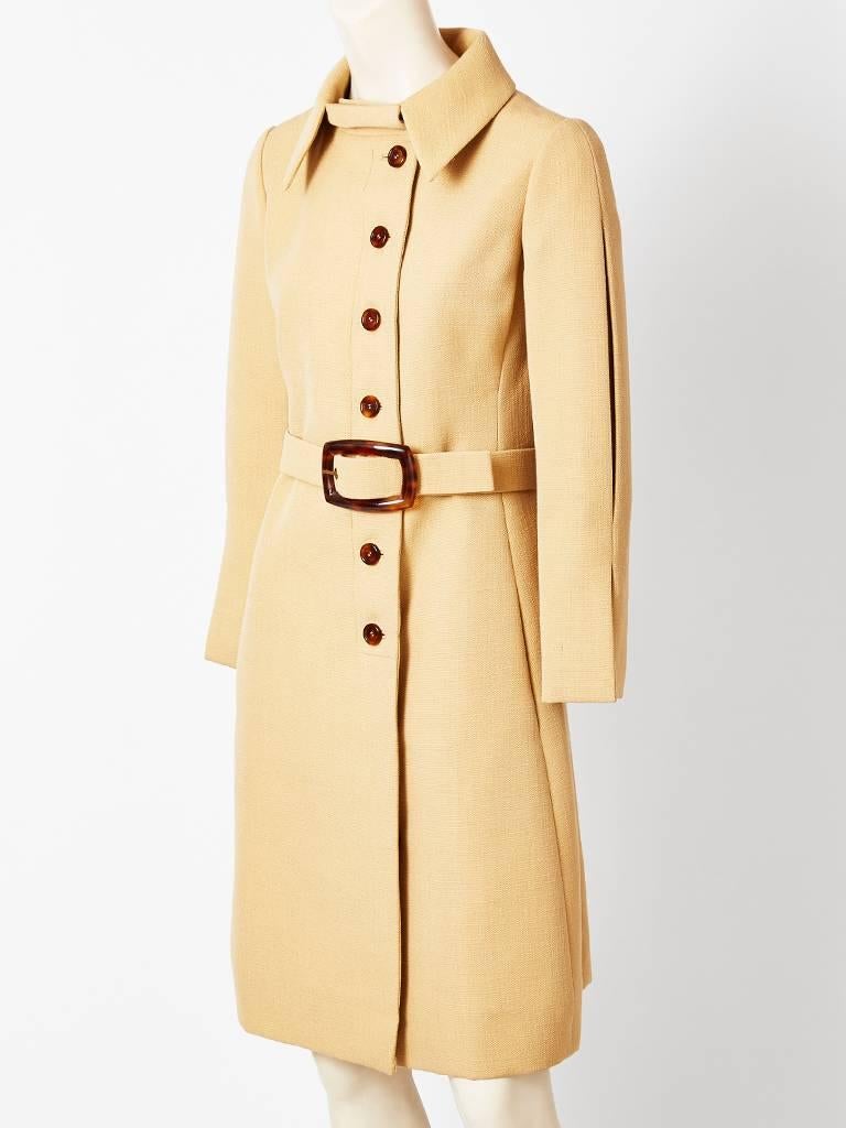 Galanos, camel tone, belted wool coat, having a pointed collar, slim silhouette, and faux tortoise belt buckle and buttons. 
