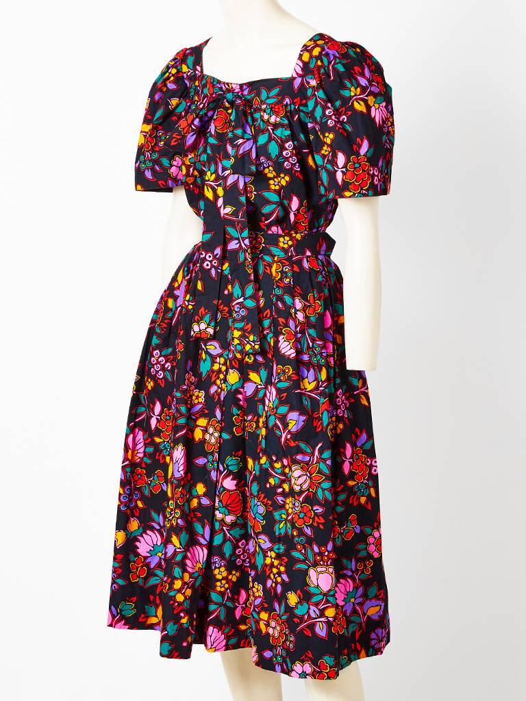Yves Saint Laurent, cotton, floral pattern blouse and skirt ensemble, having a colorful print on a black background. Smock style short sleeve top hias a center bow. Skirt has a waist band, with gathering and a side closure . Side pockets are hidden.