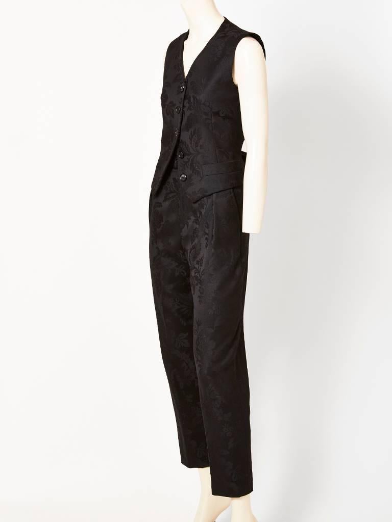 Yves Saint Laurent, sleeveleess, vest  and pant ensemble in a black damask pattern. Vest is a classic button front with pocket detail having a satin bow at the back waist. Trouser style pant, has a fly front with soft single pleats and a tapered leg.