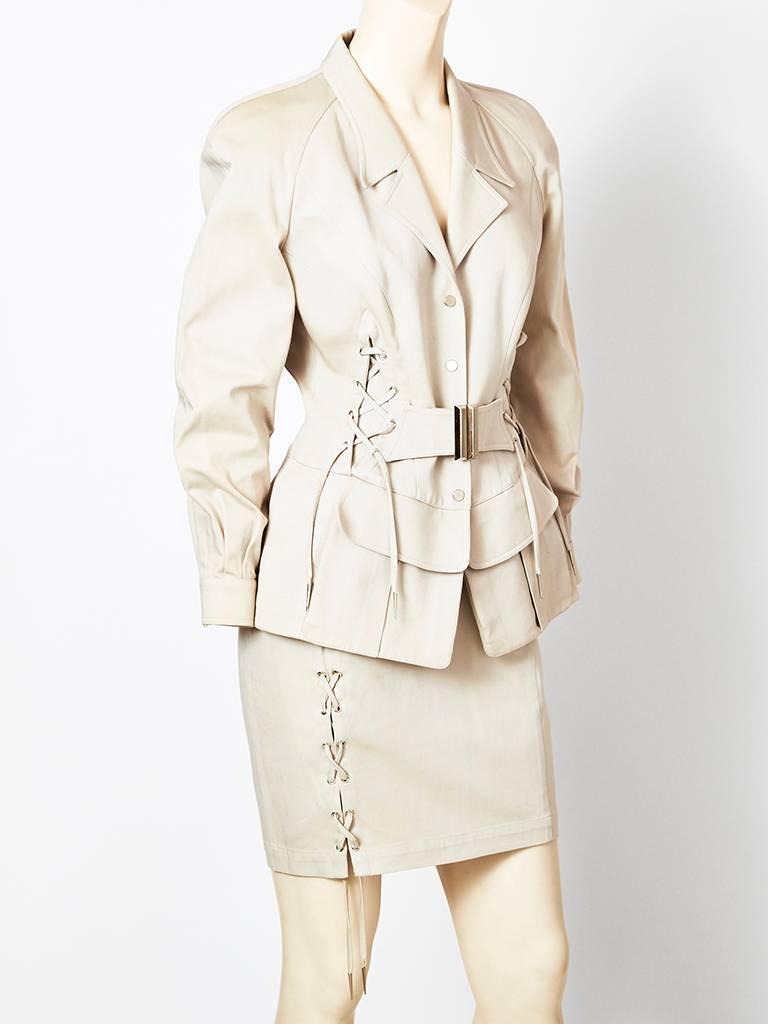 Thierry Muglar, cotton gaberdine, safari inspired skirt suit in a stone color, having a corseted waist with lacing on both sides, and a front military style belt with a chrome buckle. Notched lapel collar and flap pockets at front. Skirt is narrow