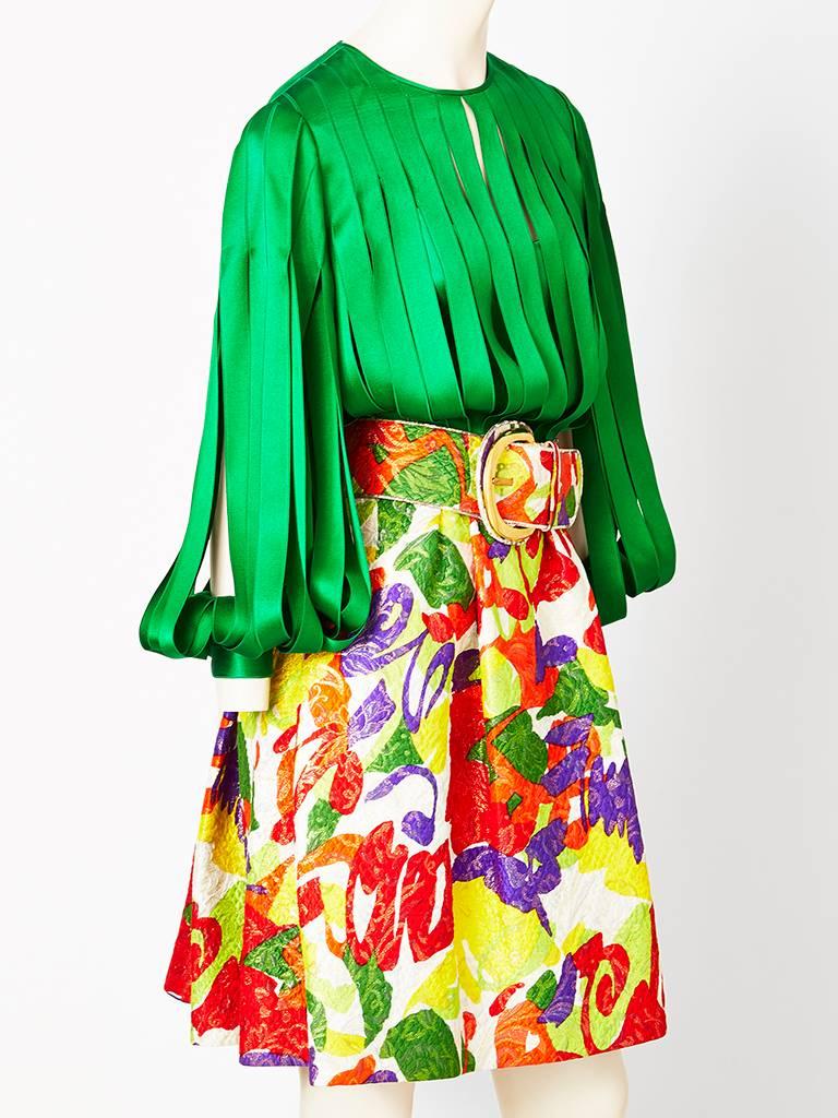  James Galanos,dramatic, emerald green and patterned brocade cocktail dress. Bodice and sleeves are silk satin, having vertical strips that look like ribbons.  Ribbon like sleeves expose the arms. The waist is gathered with a wide belt that matches