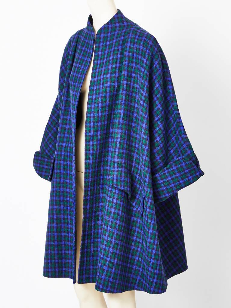 Geoffrey Beene, double face wool, swing coat in a colorful small plaid pattern in shades of navy blue, ( background) emerald green and purple. Coat has a standup Mandarin like collar, with no closures. The coat has a generous, swing shape with