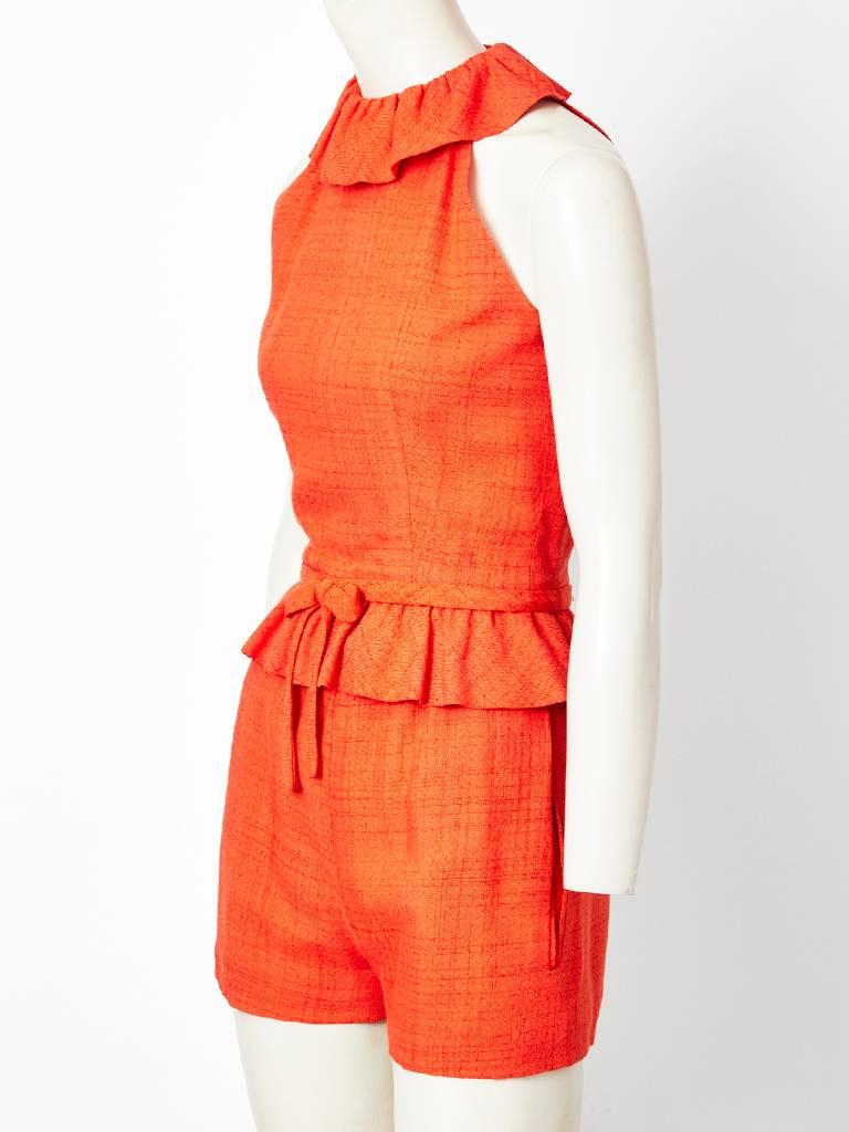 Pierre Cardin, tangerine, top and shorts ensemble. Sleeveless, halter cut shoulder with  a ruffled collar, fitted bodice and a gathered peplum having an external waist band with a center attached bow. There is a back zipper closure.
Shorts have