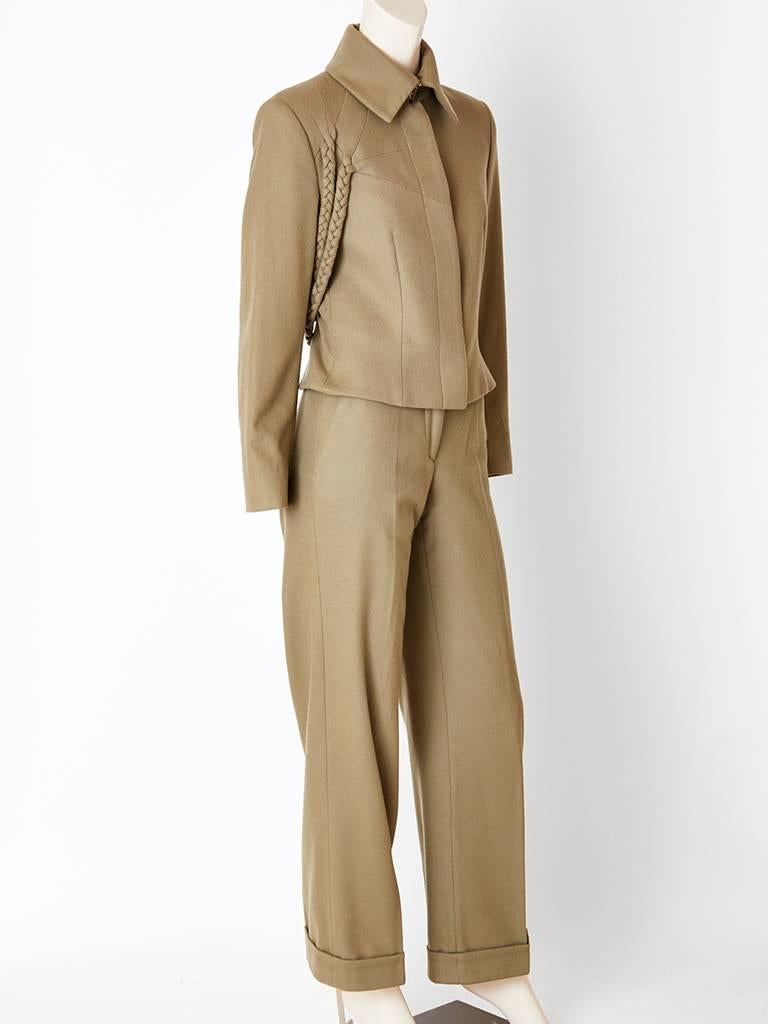 Alexander McQueen, taupe, wool flannel, pant suit , having a cropped jacket with a small pointed collar and hidden buttons closure. The jacket has a braided detail inspired by military decorative braiding often seen falling from an epaulet. The