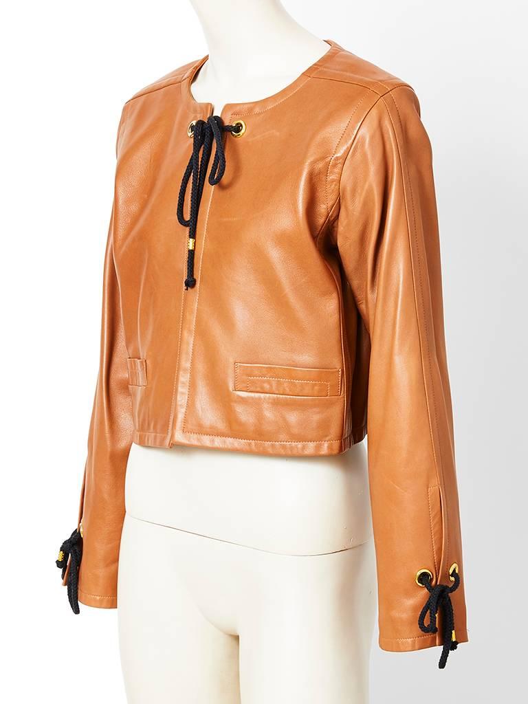 Yves Saint Laurent, caramel, tone, cropped lamb skin jacket, having  a box shape with gold grommets detail and a black cord that fastens  at the neck and cuffs. Horizontal pockets at the front.