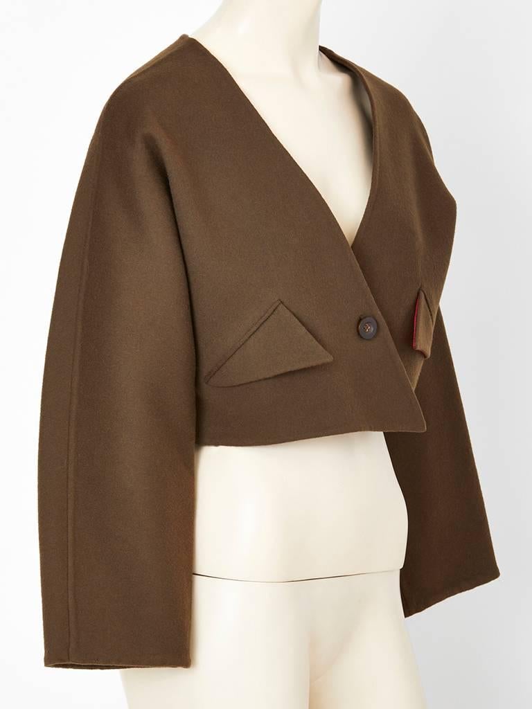 Geoffrey Beene, chocolate brown, double face wool cropped jacket, having a collarless, V neckline, with a pointed geometric detail at the front closure. Flap pockets echo the point with red lining peeking out. Single button closure.