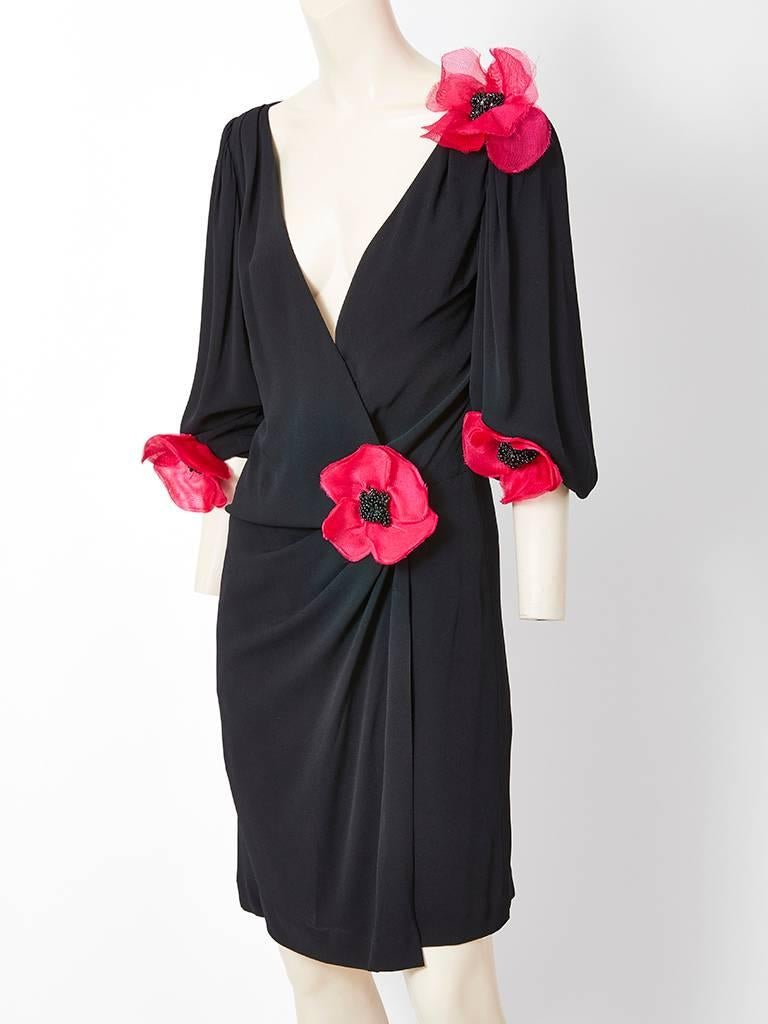 Yves Saint Laurent, black jersey dress having a deep V neck that fastens at the side hip with draping below the waist. Balloon sleeves end at the elbow. Dress is embellished with red organza poppy flowers at the side of the waist, shoulder and