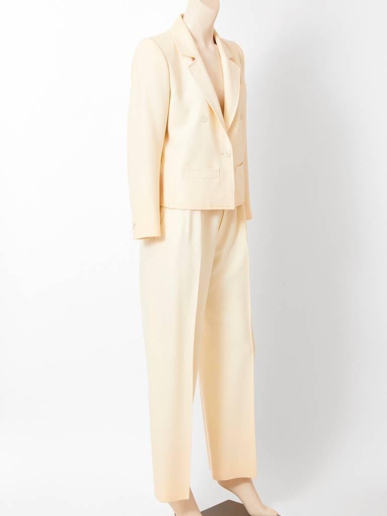 Yves Saint Laurent, Rive Gauche, ivory tone, wool gaberdine, pantsuit, having a box style, jacket, narrow notched lapels with horizontal, front, slit pockets and a single button closure. Trousers are menswear style with pleats and a fly front.