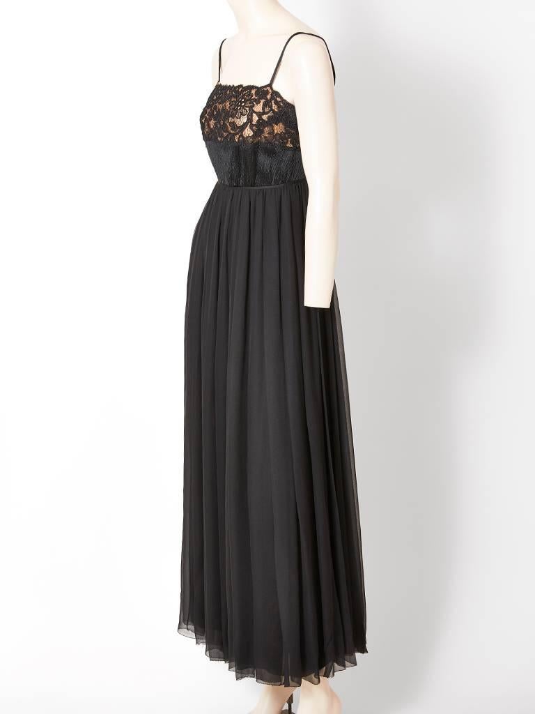 Galanos, black evening gown, having a layered chiffon skirt with a slightly empire waist.  Bodice is hammered satin and Guipure lace. The lace is placed over the bust line having a lining in nude chiffon. There are thin satin tubular straps and an