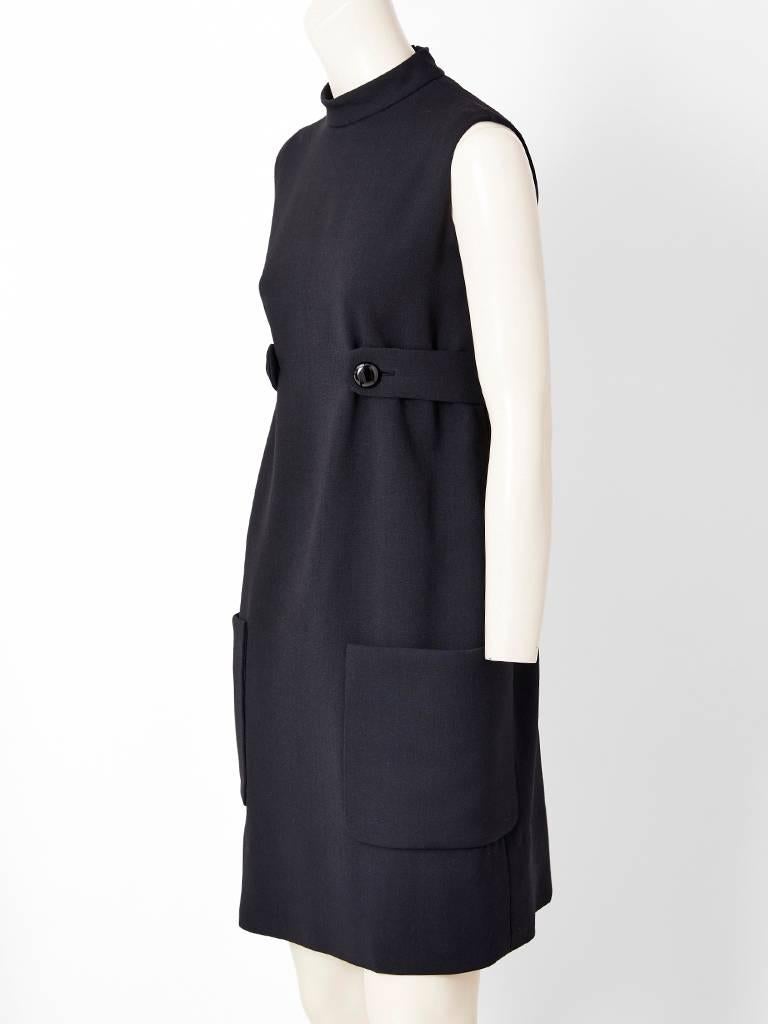 Classic Norell, black wool, sleeveless sheath, having a high neckline, slightly empire waist with a half belt attached by buttons and low placed, deep patch pockets detail. ( Missing Label ).