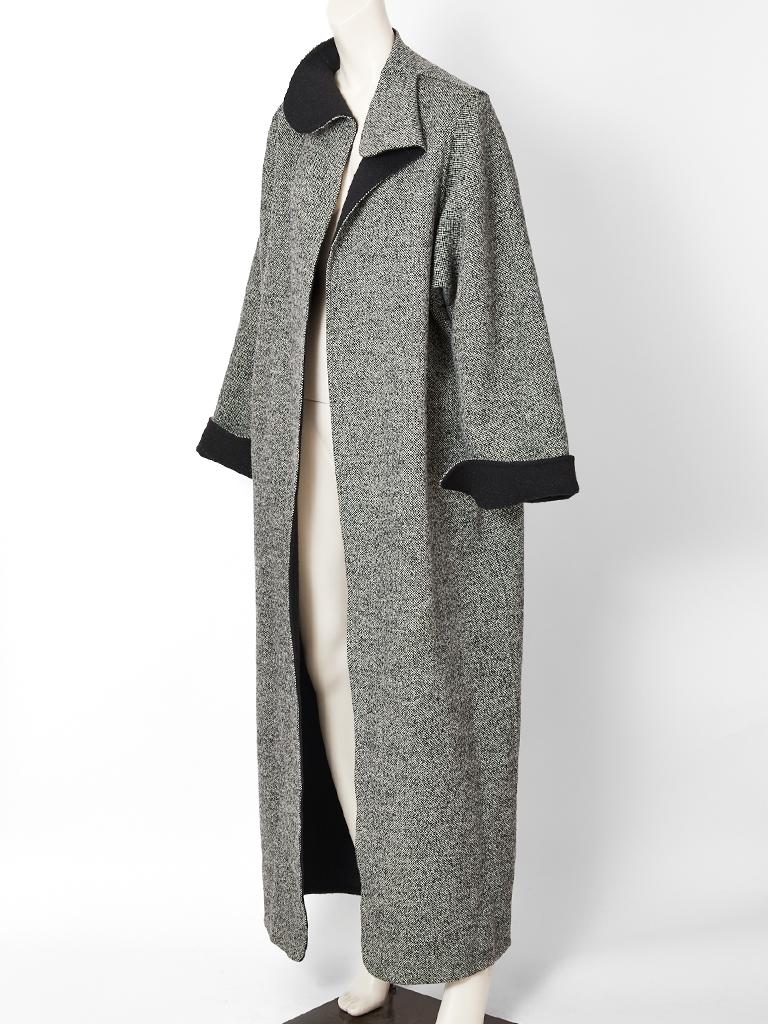 Geoffrey Beene, double face wool, straight line, maxi coat, having a black and white tweed exterior, and a black wool interior. There is a stand up collar that falls softly at the chin. Sleeves can be cuffed at the wrist to expose the black interior.
