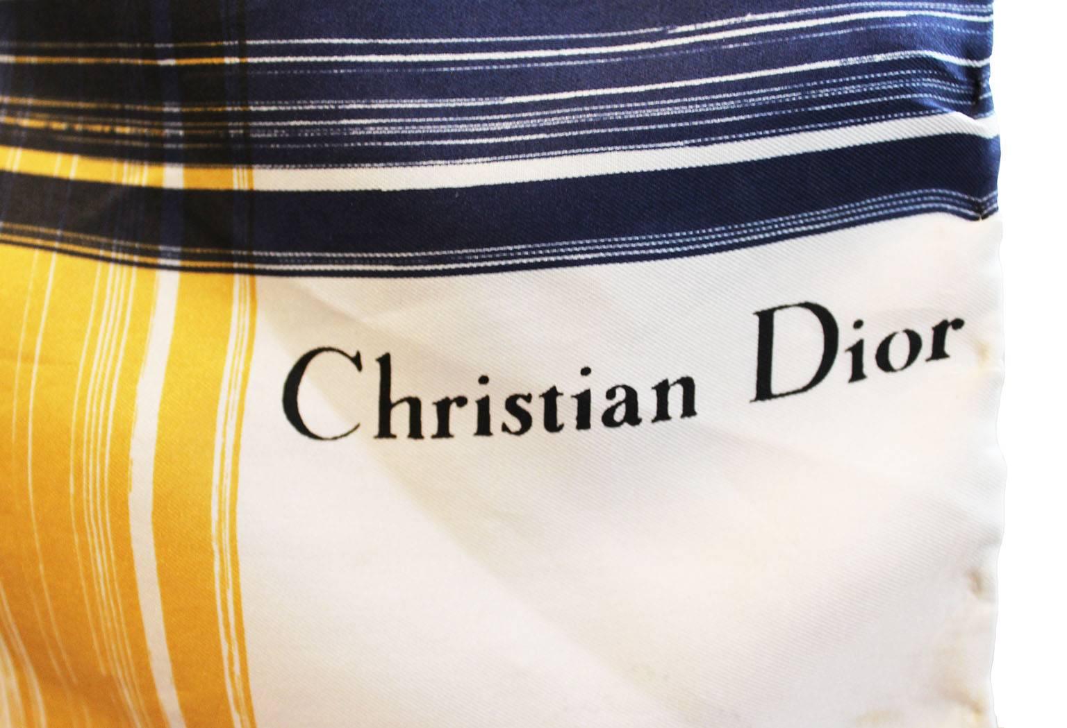 A chic silk scarf by the French designer Christian Dior.
In an interesting linear design, with mustard yellow stripes of varying widths running vertically, and blue stripes of varying widths running horizontally. The background is ivory in colour