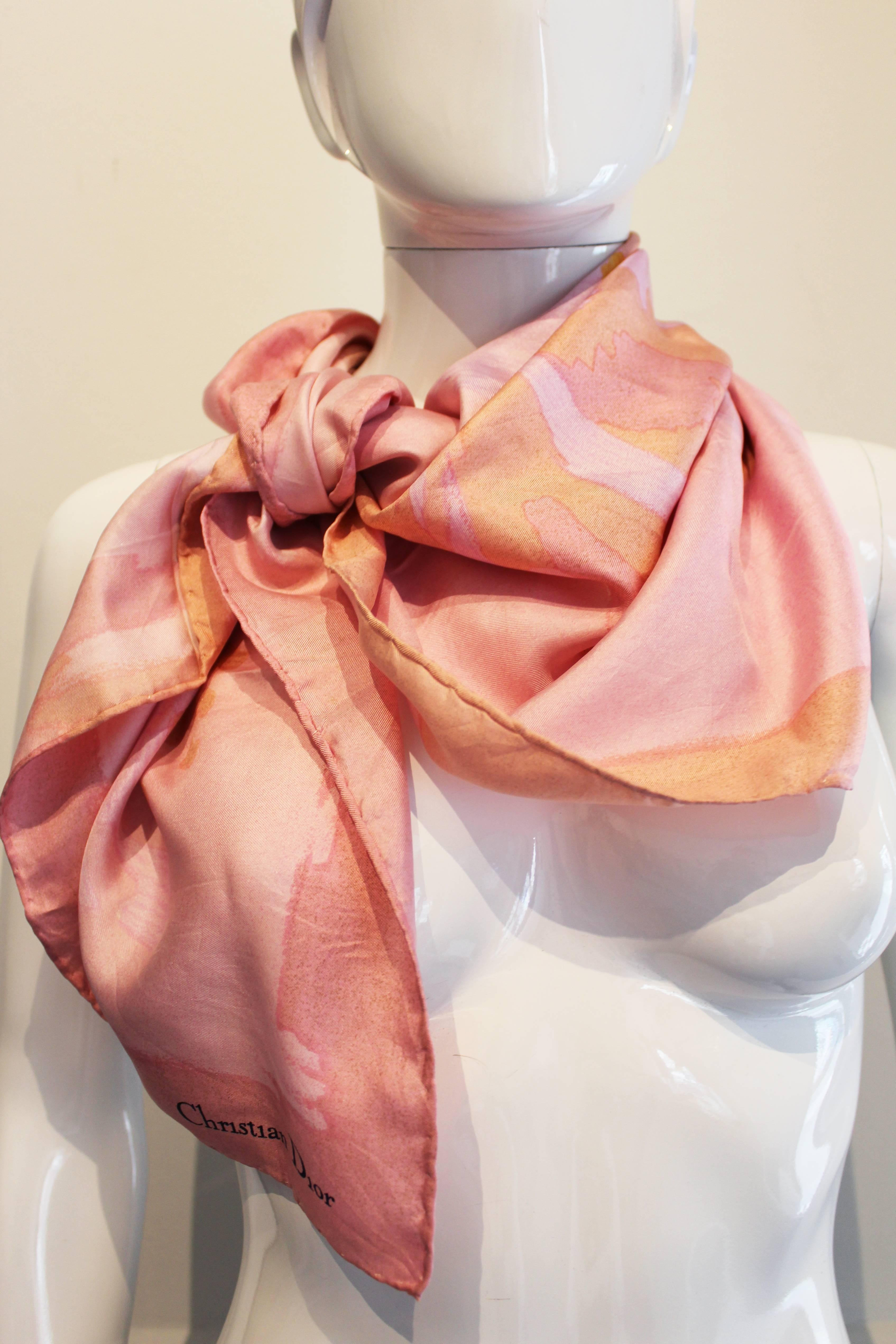 A lovely scarf for Summer.This is a pink silk scarf by French house Christian Dior. The scarf has a duty pink border, with a paler pink centre and an abstract floral design in yellow , pale orange and biscuit. As you would expect from Dior the silk