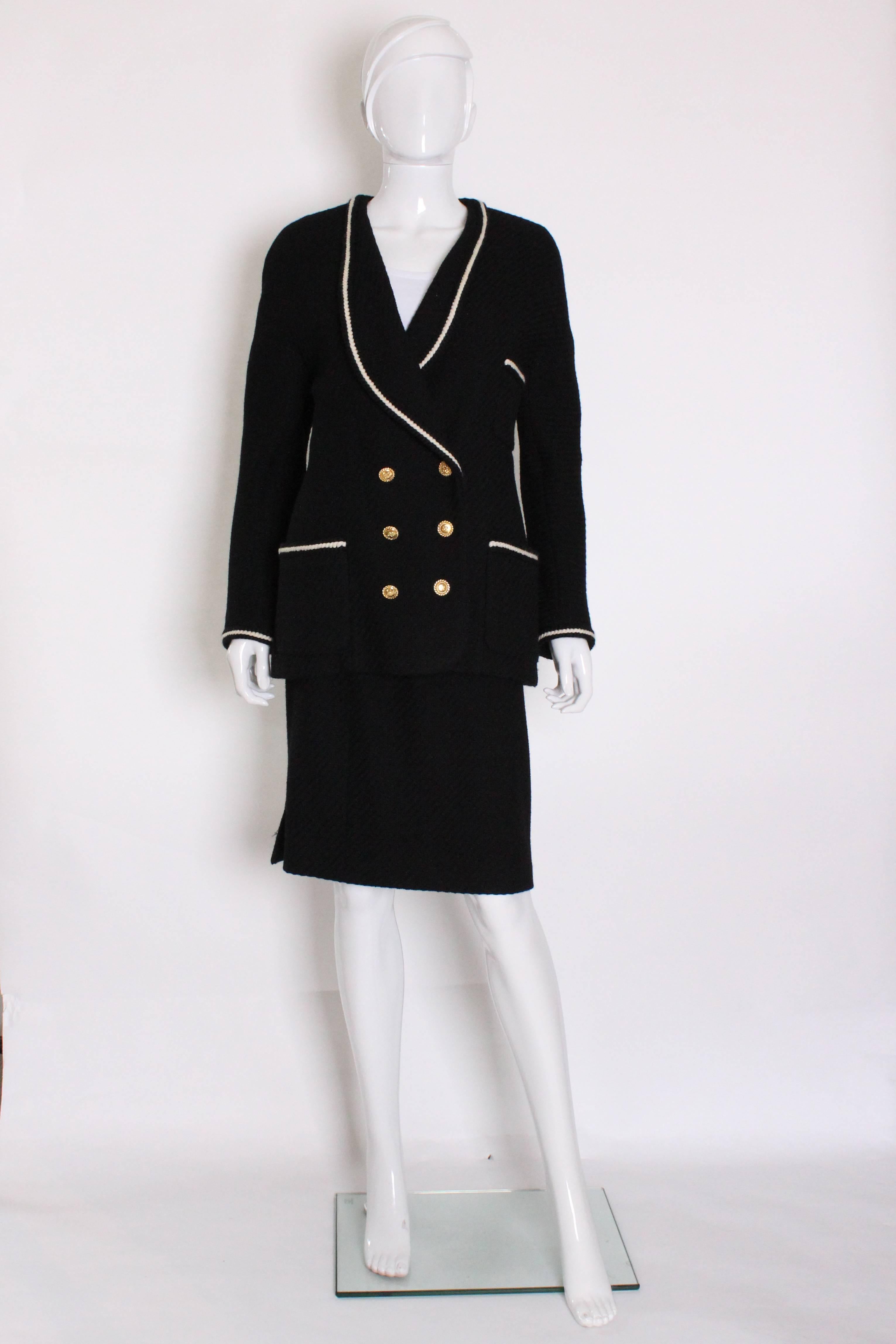 

A charming and chic skirt suit from the French house of Chanel.
The jacket is black with white trim. It has a narrow shawl collar with 2 hip level pockets and one breast pocket.It is double breasted with 6 buttons on the front and 4 on each