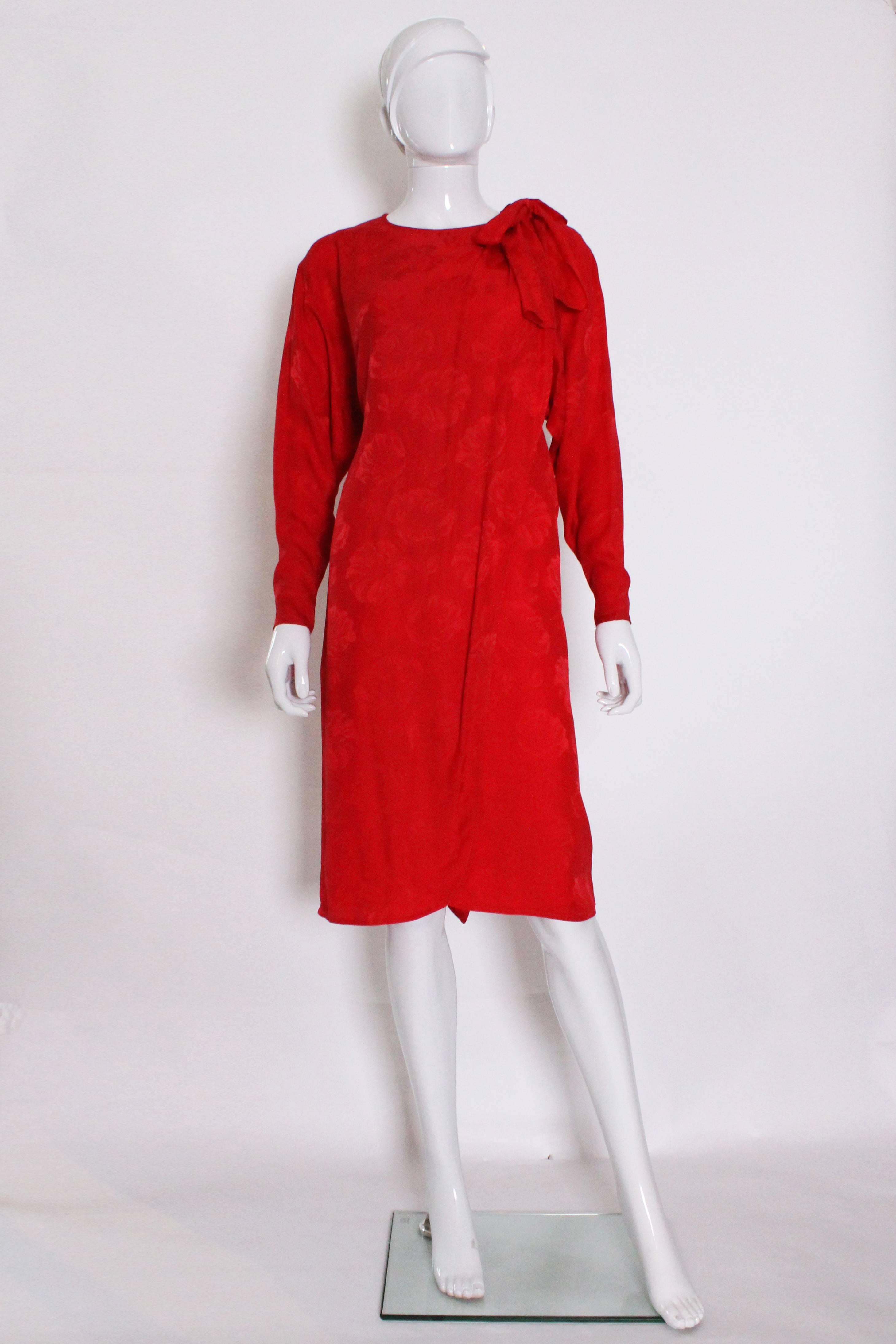 A chic cocktail dress from the French house, Christian Dior . The fabric is  a red silk with flower pattern.The dress is carefully constructed with an internal column ,and 'wrap over ' at the front and back.
The back wrap, has three pleats on the