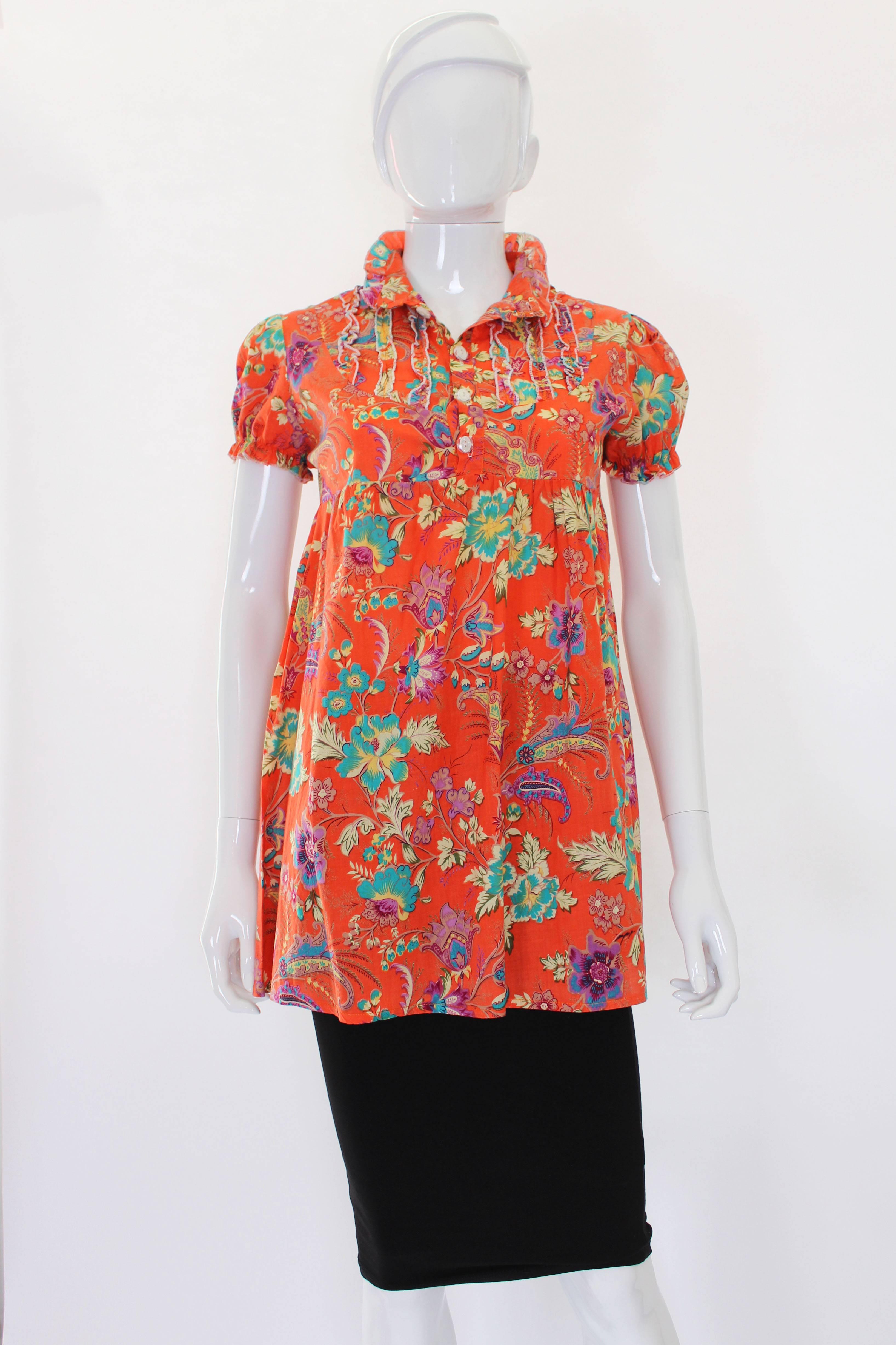 This blouse is made of a soft light wieght cotton with a colourful floral print on an orange background. The blouse is in a baby doll style shape. It has a small stand up collar that sits around the neck when the buttons are done up but can be worn