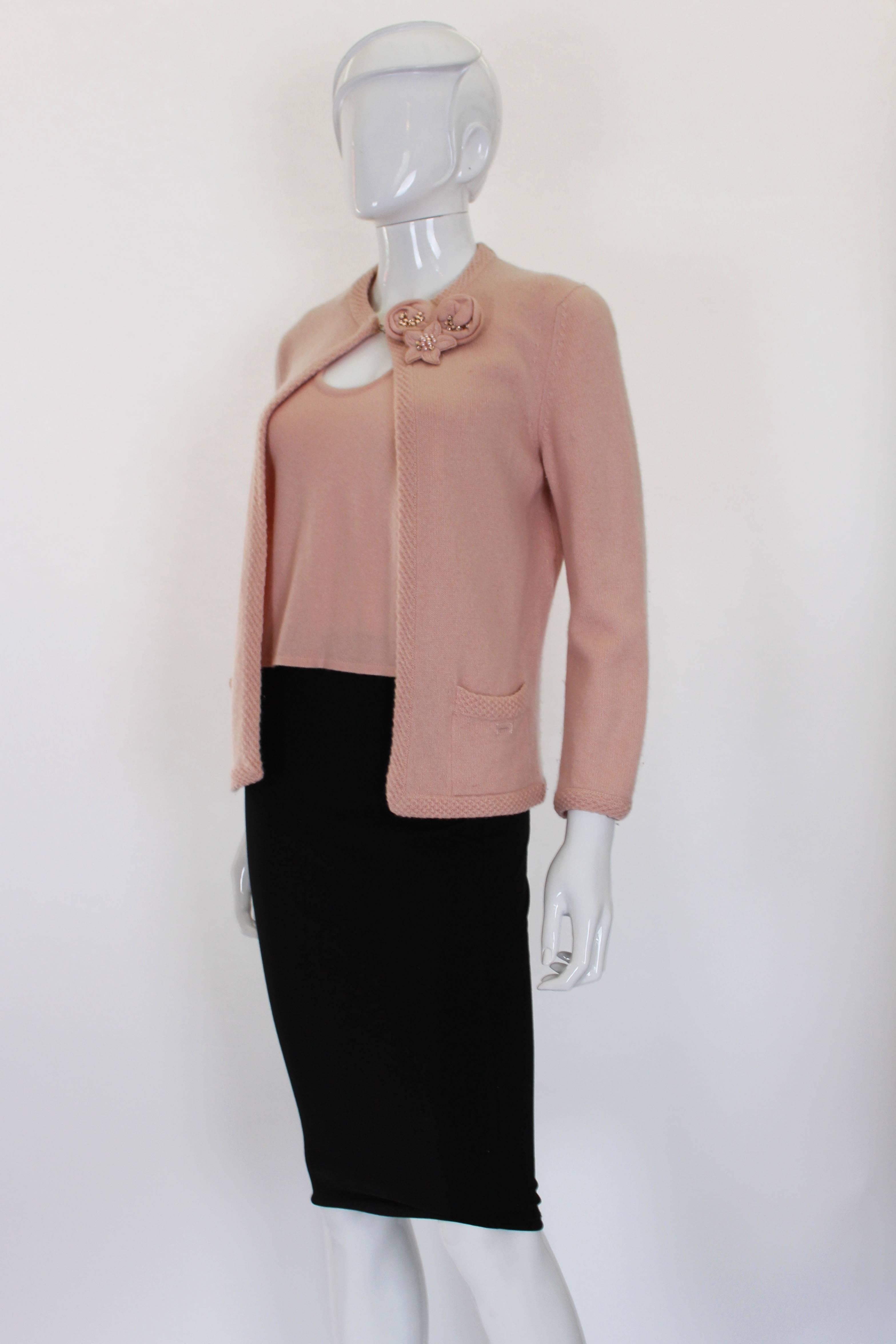 This Chanel 2 piece is made up of a cashmere tank top, matching cardigan and 3 floral broaches. Each of the broaches is made of the same dusty cashmere, with crystals in the centre. The broaches can be removed or placed anywhere on the piece. The