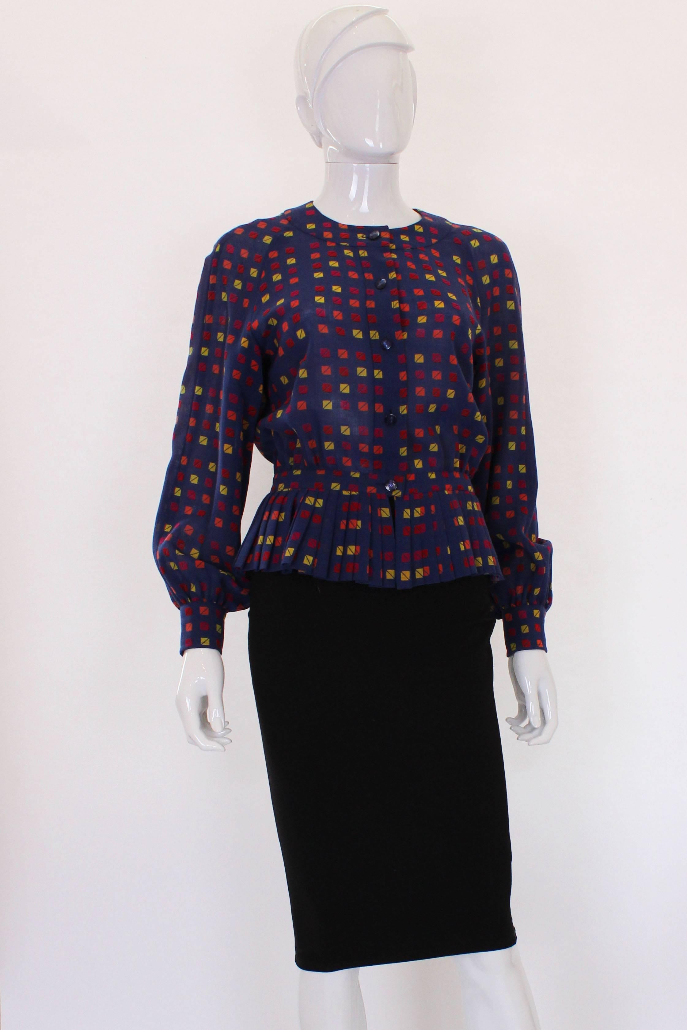 A great top for fall. This top is by French design house Celine,It is 100% wool, with a mauve background and a print in squares of yellow, pink, orange and red.It has a round neck, button front and pleated peplum . There is a 5 button opening at the